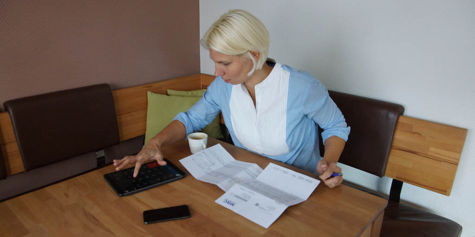 Eine Frau sitzt am Tisch mit Dokumenten und einem Tablet